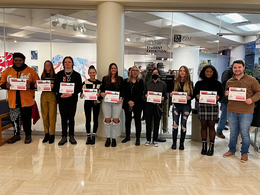 Group of 9 Art students holding their certificates along with the department chair person positioned in the middle of the line up.